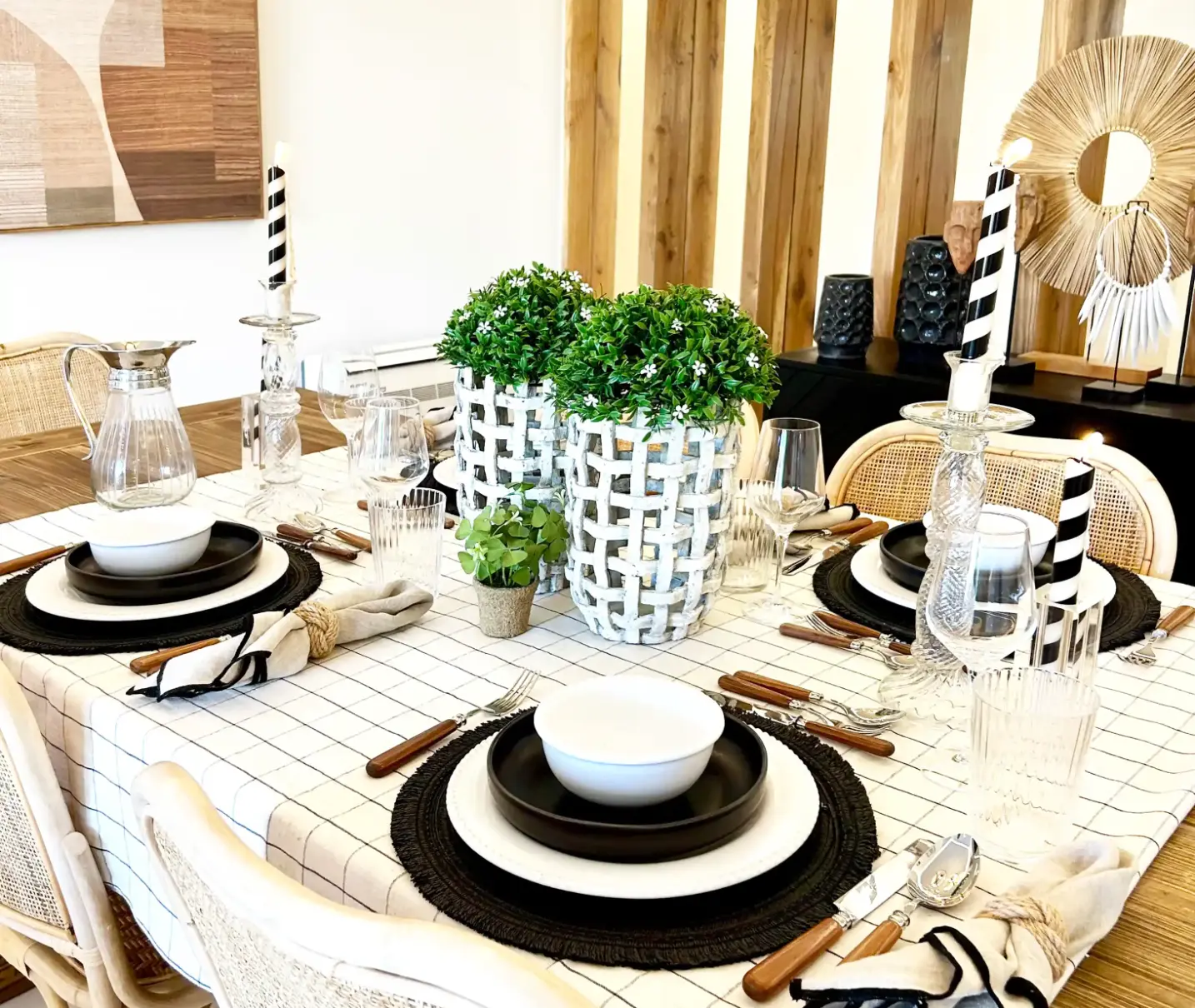 Decoração de mesa de jantar com pratos brancos e pretos,  toalha de quadrados, arranjo floral central e velas pretas e brancas